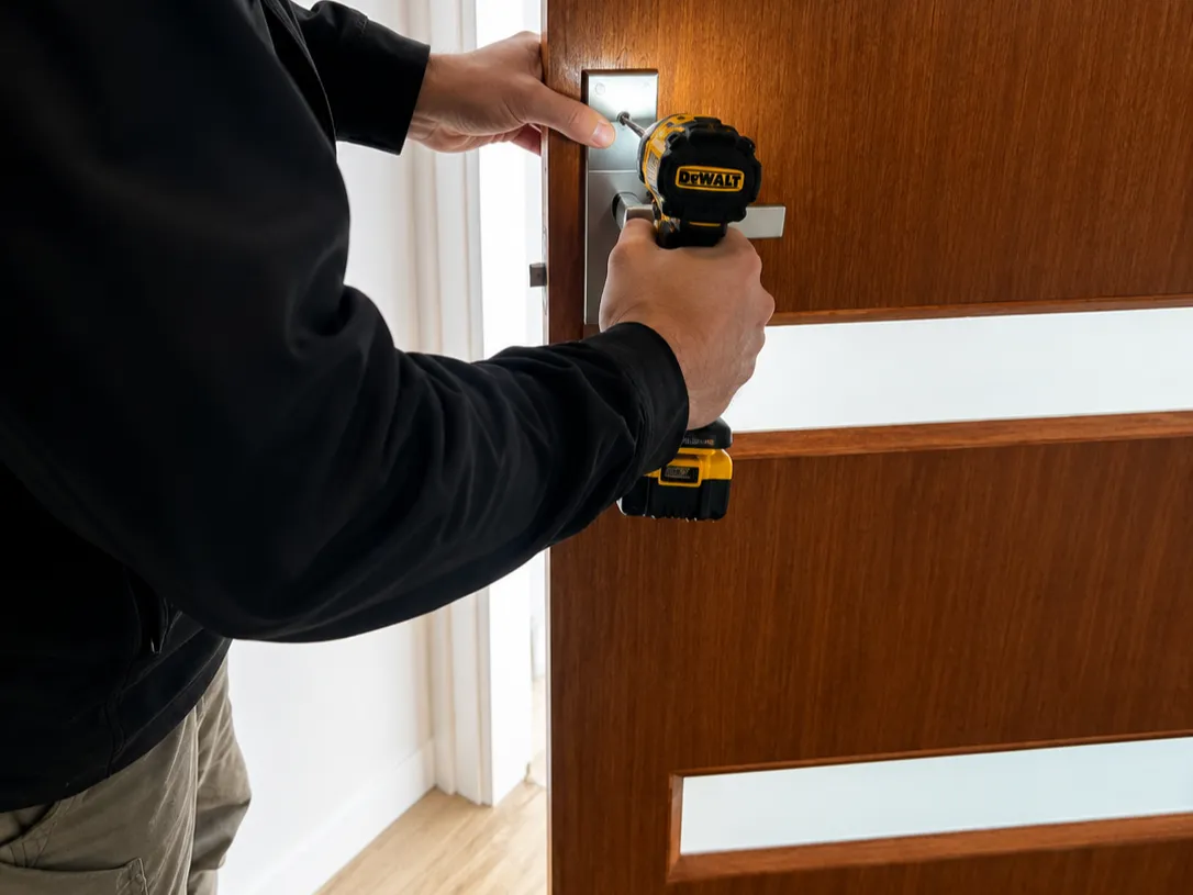 Locksmith fitting a new lever handle to a timber door with a drill